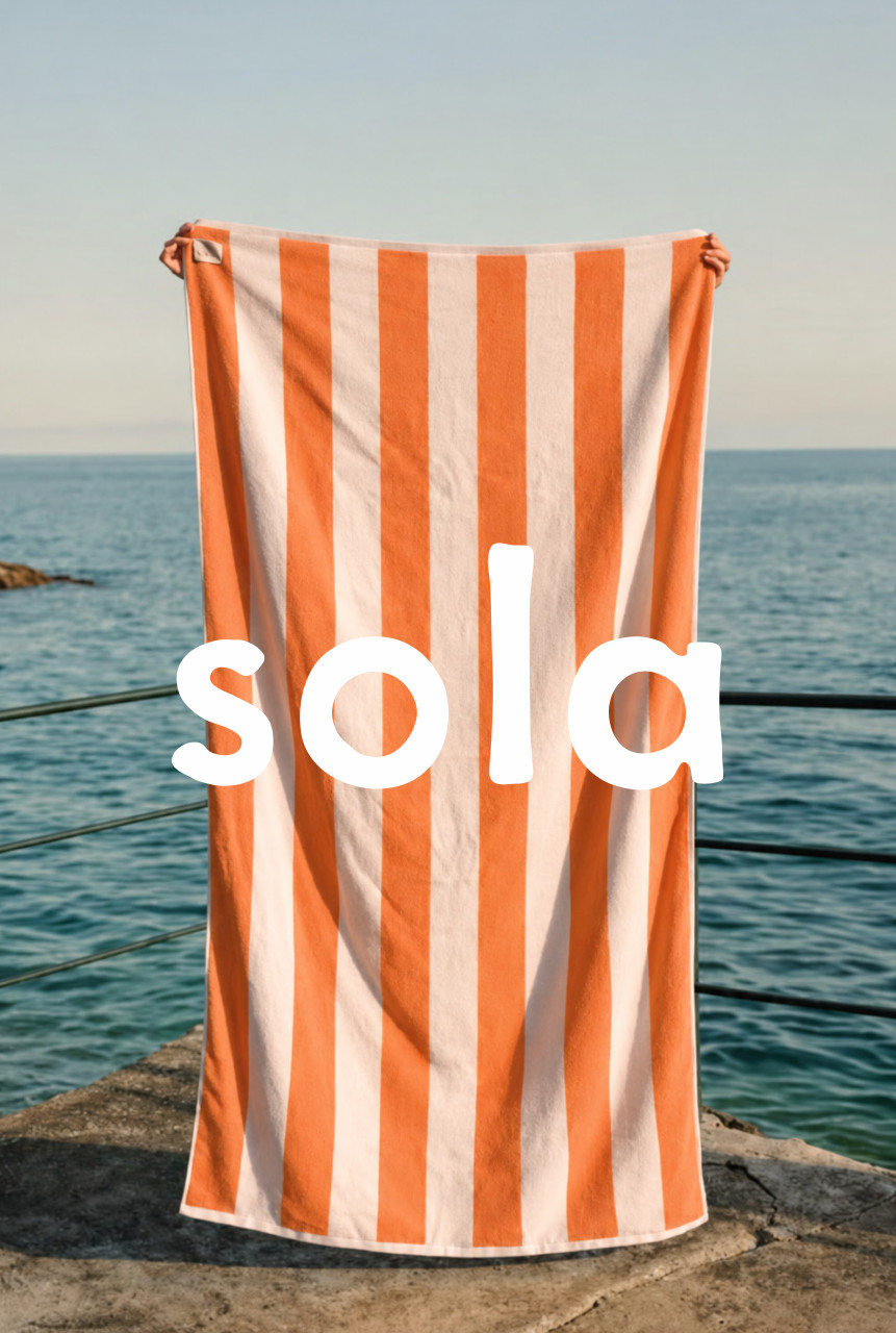 Orange and cream striped Sola beach towel beside the ocean